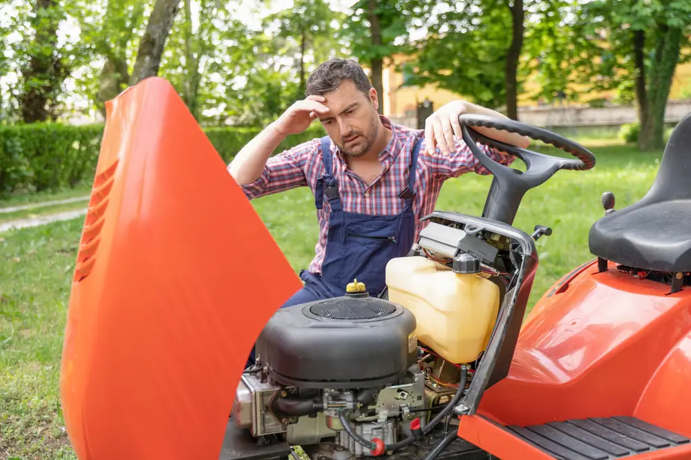 A man looking at his riding lawn mower engine and wondering what to do.