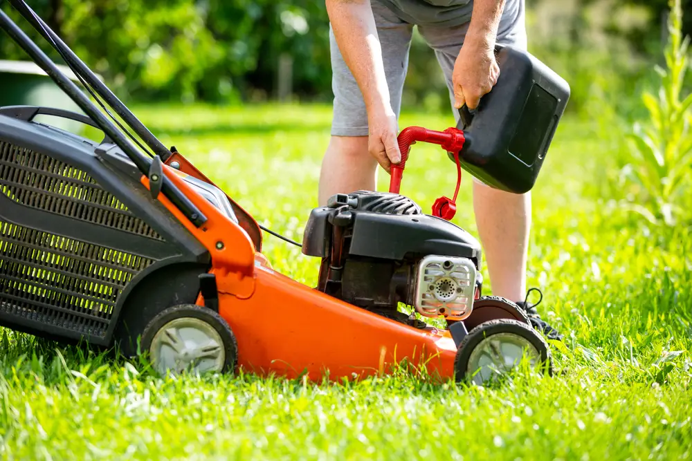 Someone pouring gas into a lawn mower.