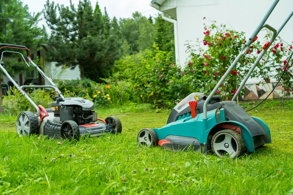 Two different types of lawn mowers facing one another in a yard.