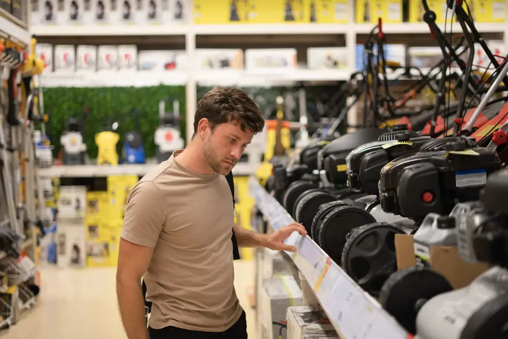 Man in a store thinking about how to choose a lawn mower.