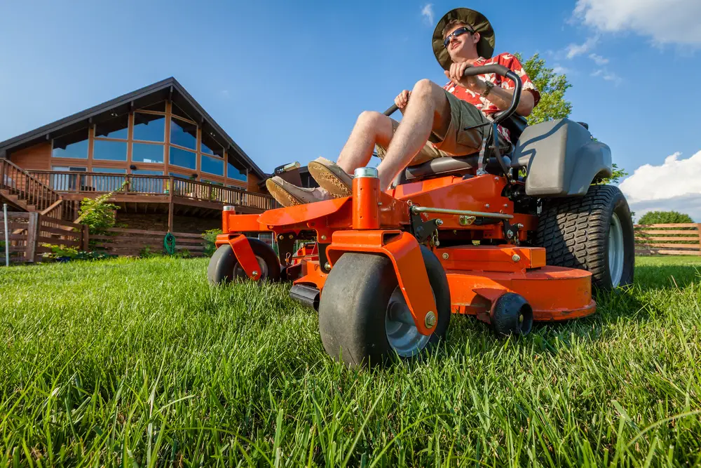 Man sitting in a riding lawn mower as he cuts the lawn.