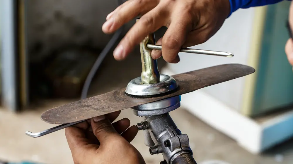 Closeup of someone working with a lawn mower blade.