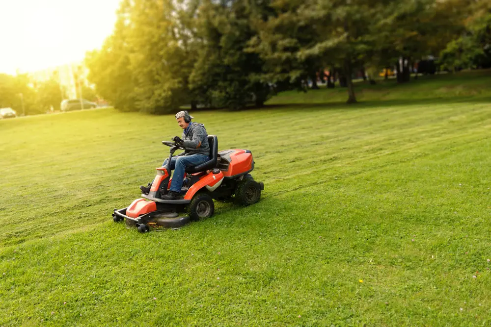 Man mowing straight lines with a riding lawn mower.