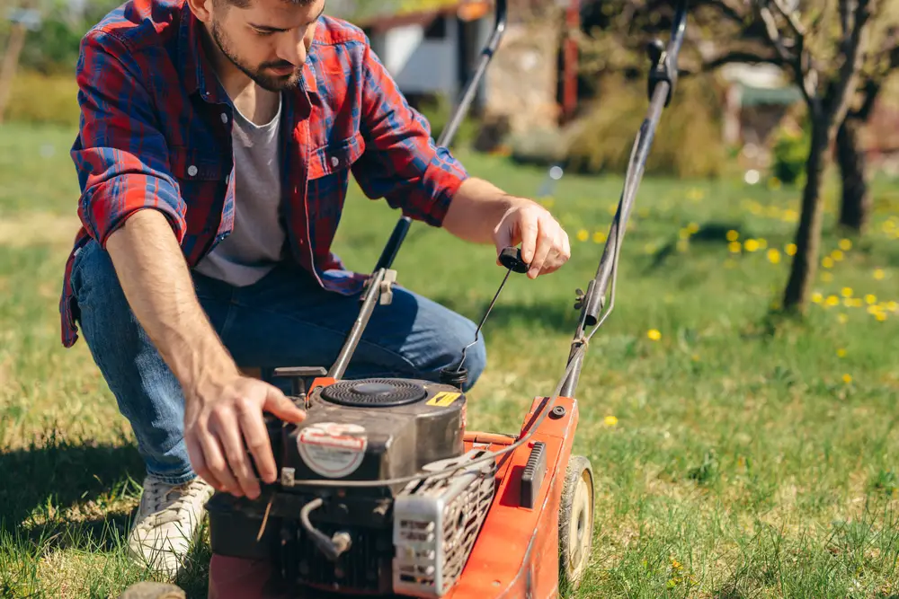 A man checking the oil level in his lawn mower with a dipstick.