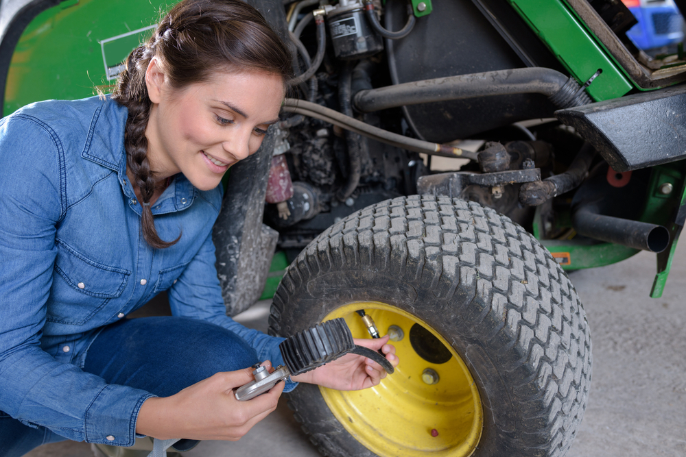 Woman measuring the air pressure of a lawn mower tire.