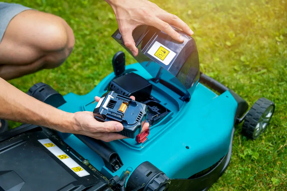 Closeup of someone about to put a battery into a lawn mower.