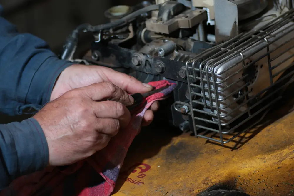 A closeup of a man starting to work on his lawn mower.