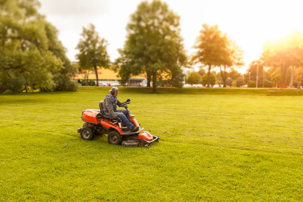 Man in the middle of mowing straight lines with a riding lawn mower.