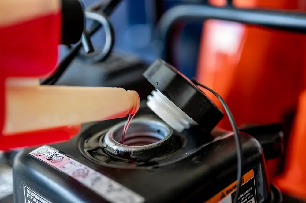 A closeup of someone adding some fuel stabilizer to their lawn mower.