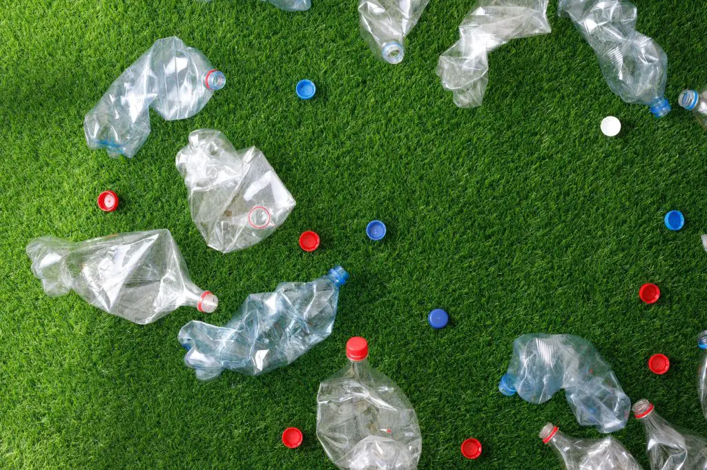 An overhead shot of plastic bottles and their caps on a lawn.