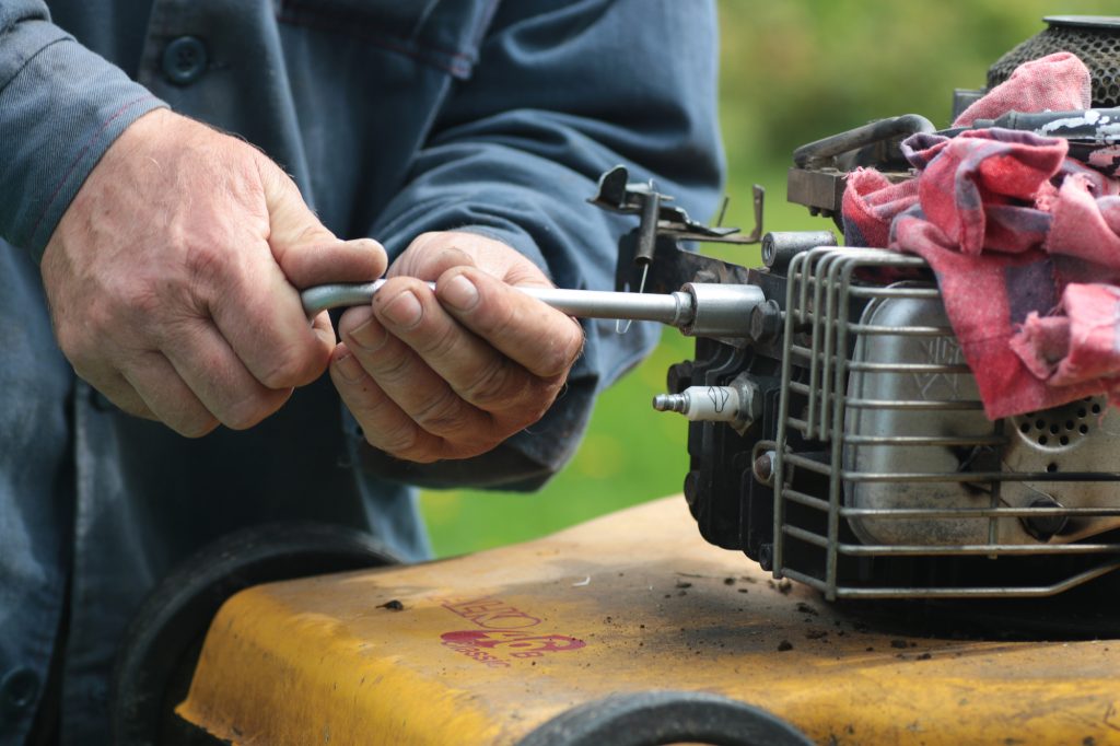 A closeup of a man working on his lawn mower.