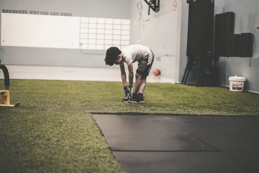 A kid stretching on artificial grass at a gym.