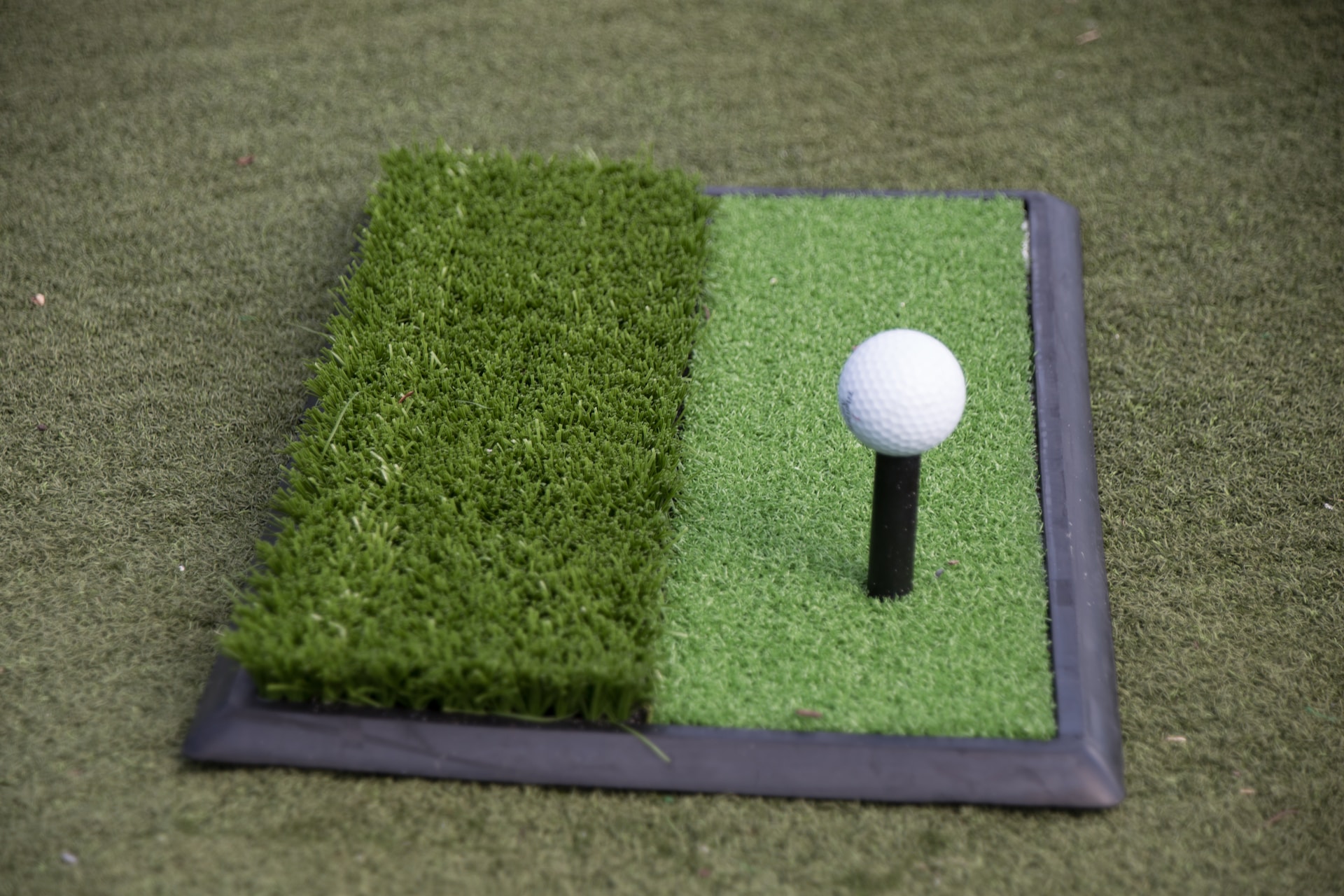A golf ball and tee sitting on a square of artificial grass.