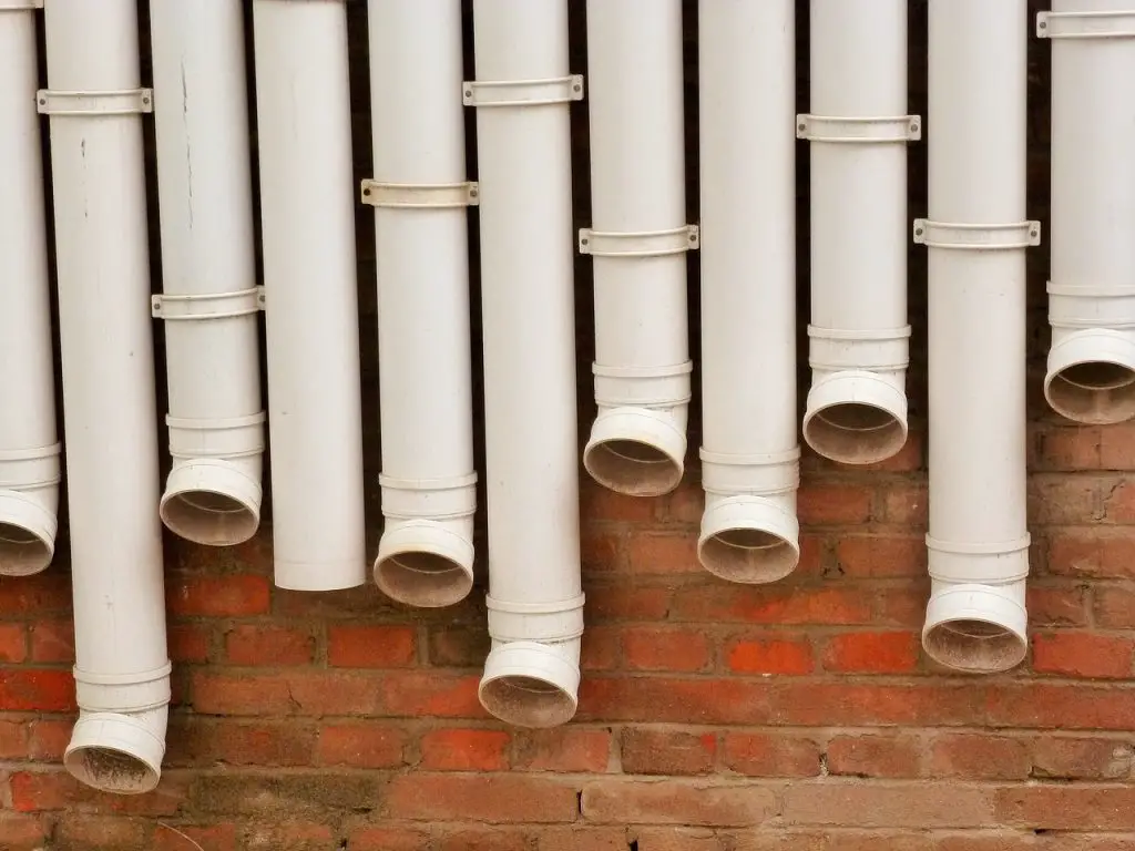 A row of downspouts against a brick wall.