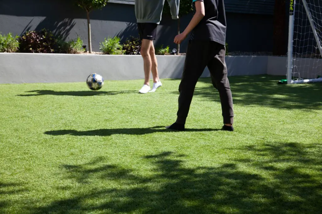 Two people playing soccer in their artificial grass backyard.