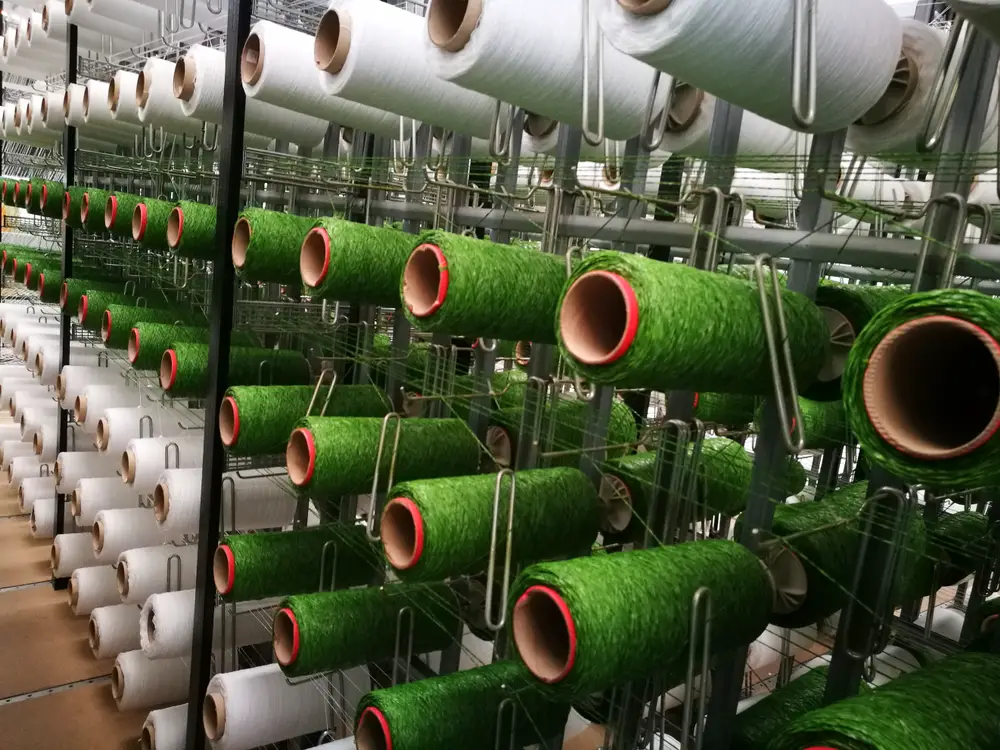 Rolls of green and white yarns for artificial grass in a factory.