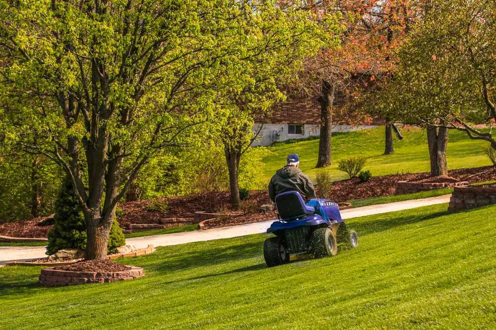An old man mowing a hill with a riding lawn mower.