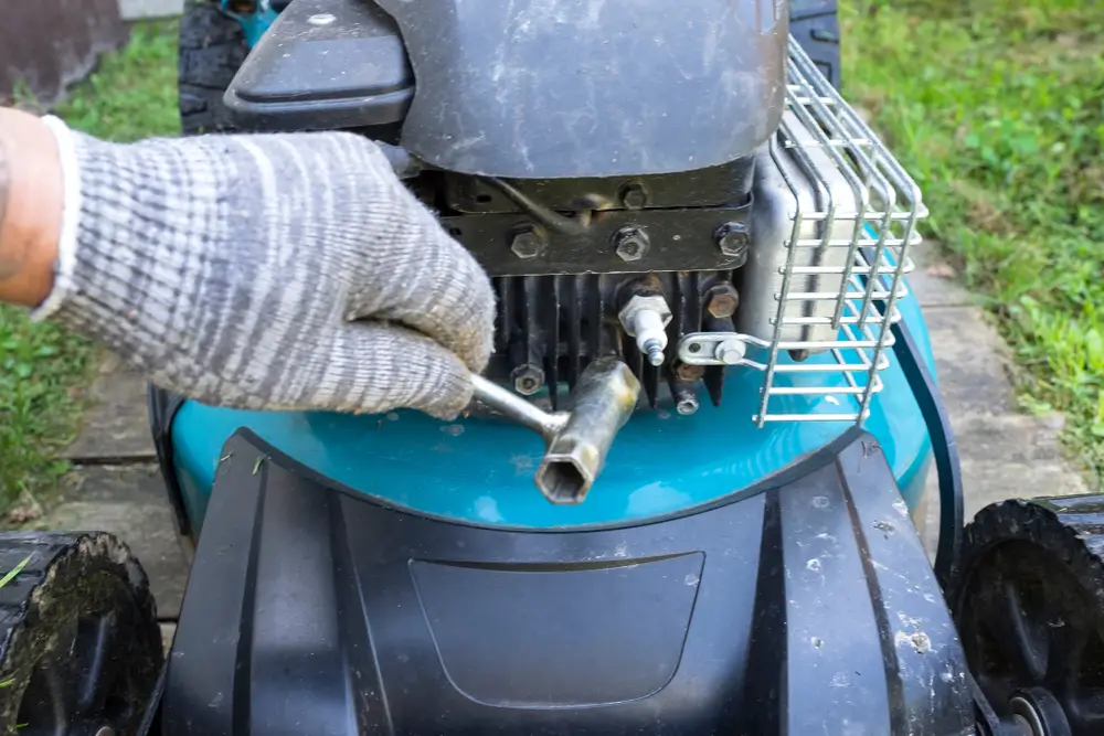 A person about to remove a spark plug from a lawn mower.