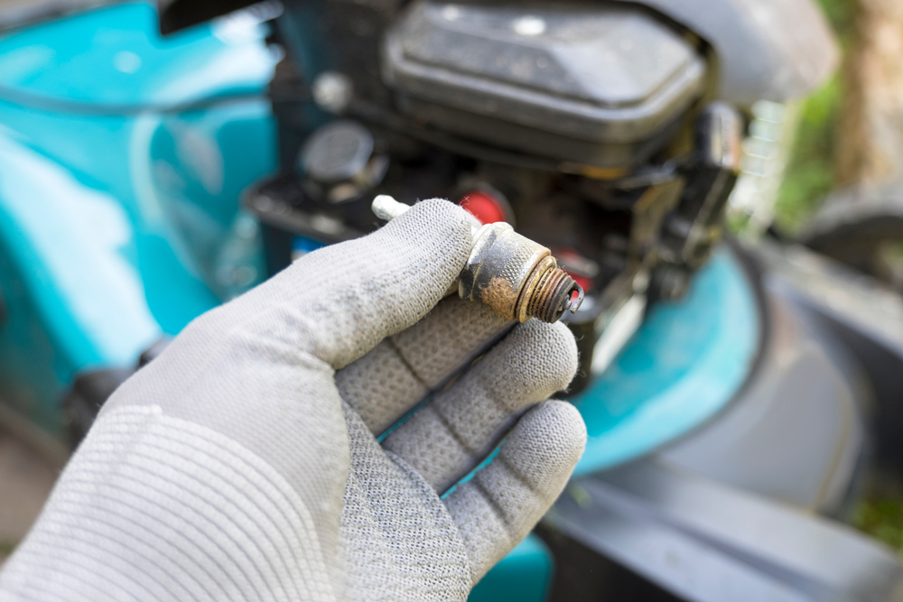 A closeup of someone holding a lawn mower spark plug.