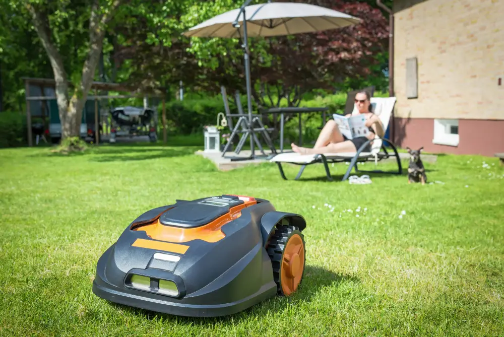 A woman relaxing in the background reading while a robotic lawn mower cuts her lawn.