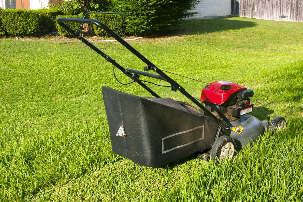 A red lawn mower with a grass bagger outside on a sunny day.