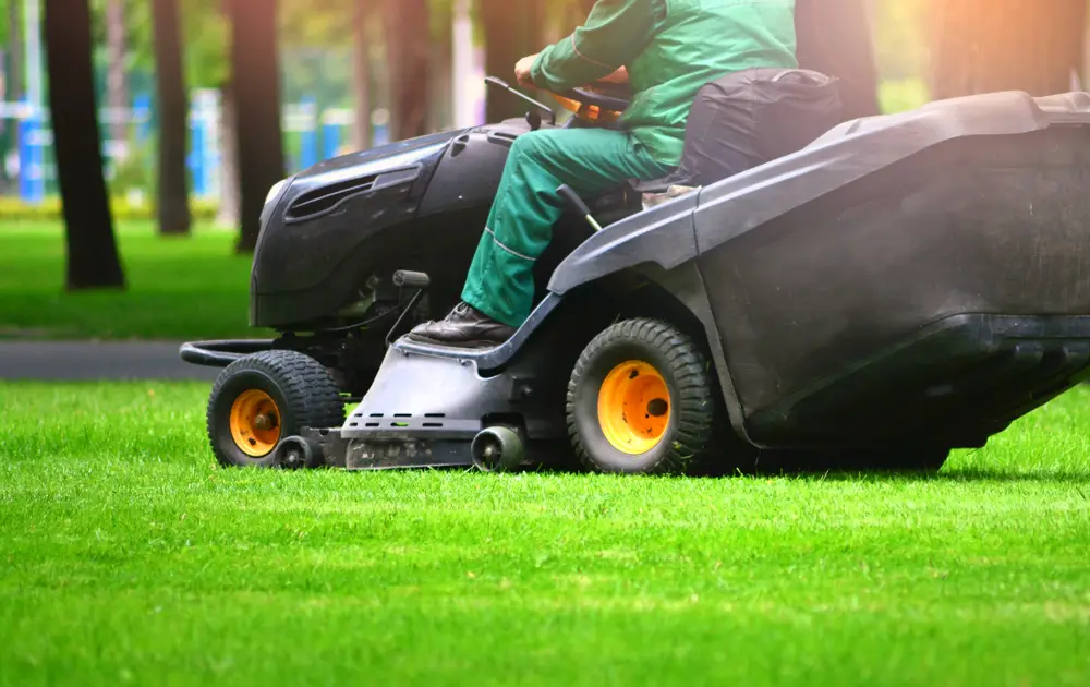 A man in a green shirt and pants cutting a lawn with a black riding lawn mower.