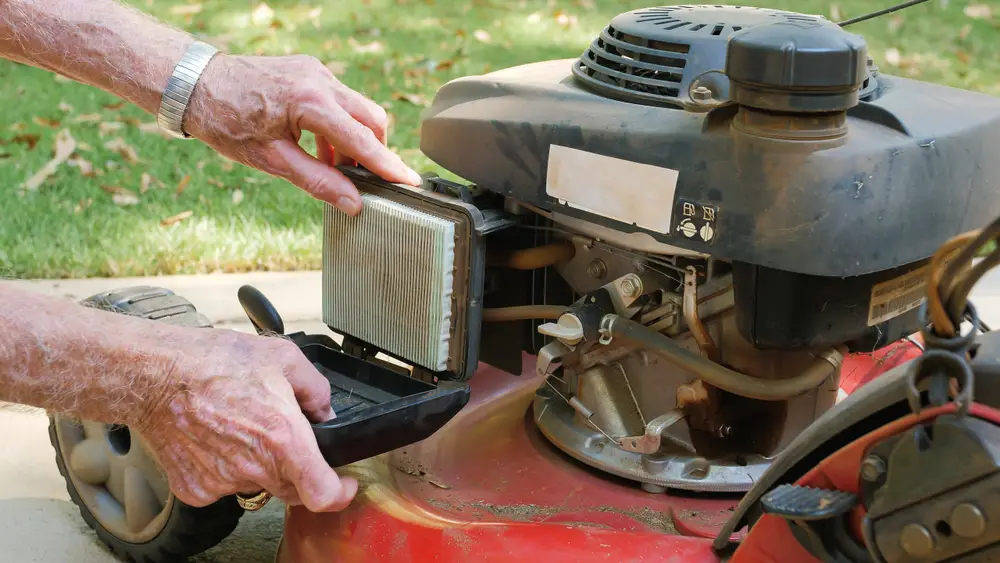 An elderly man opening the air filter on a lawn mower.