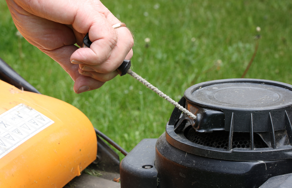 A closeup of a man pulling a lawn mower starter cord.