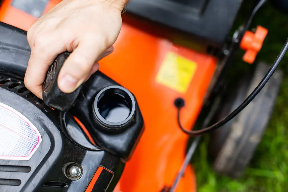 A closeup of someone inspecting their lawn mower fuel tank by lifting the gas cap.