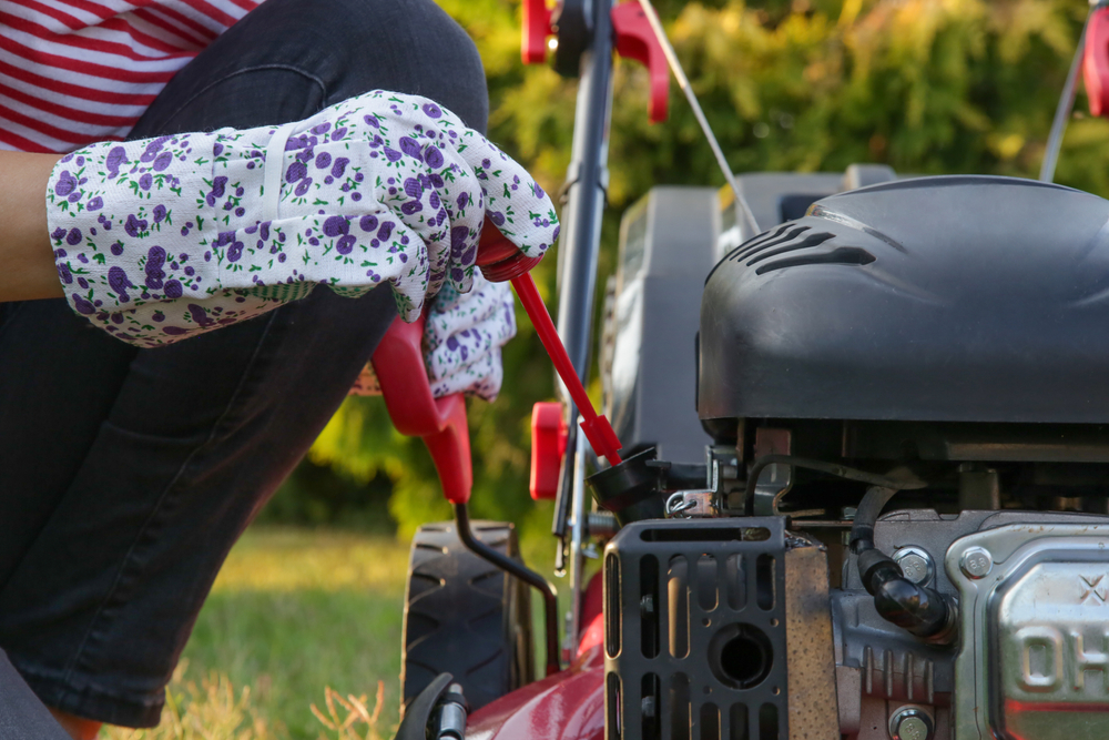 A closeup of a woman inspecting the oil level of her lawn mower.