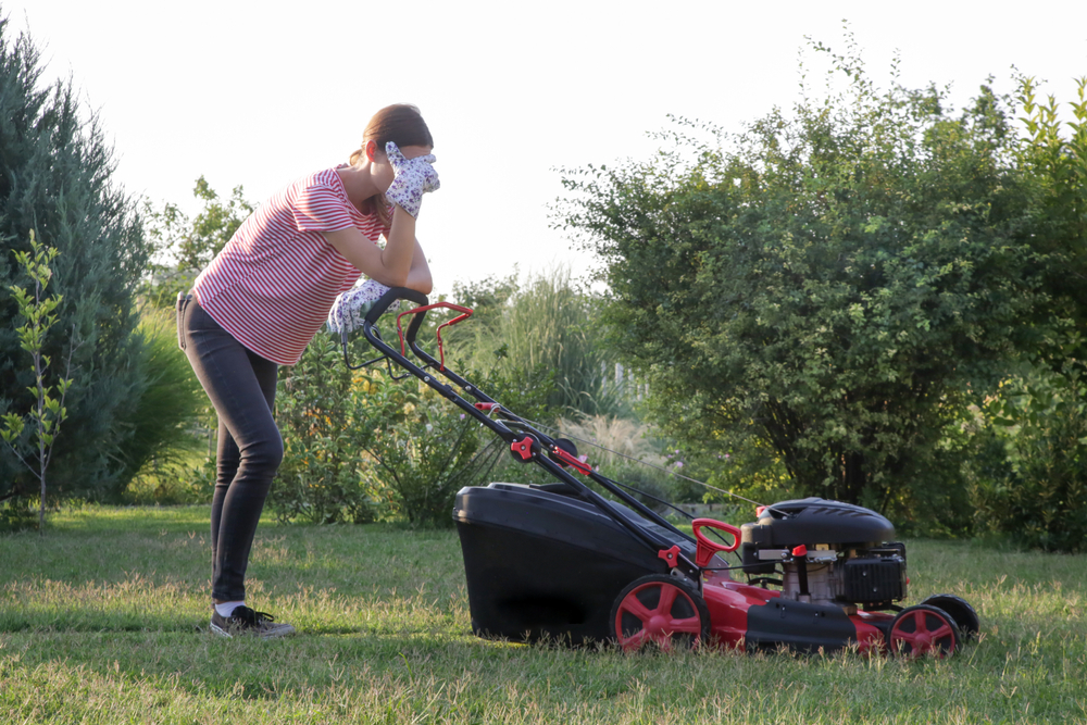 An upset woman leaning on her lawn mower.