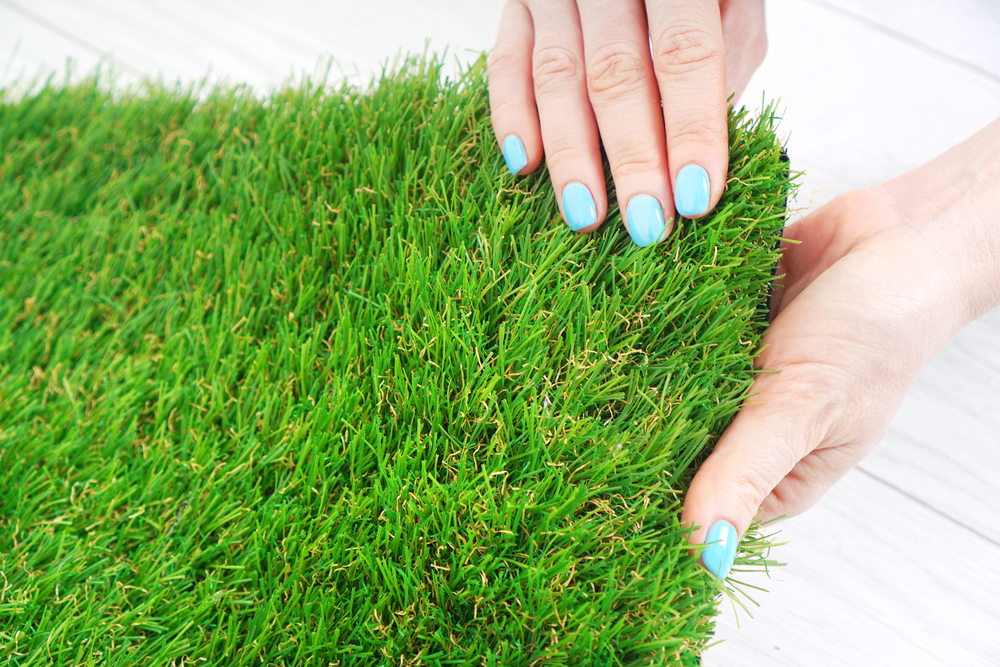 A closeup of a woman holding and feeling a patch of artificial grass.