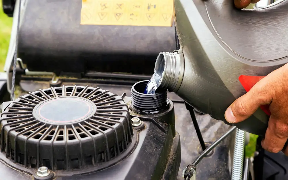 Someone pouring gasoline into their lawn mower.