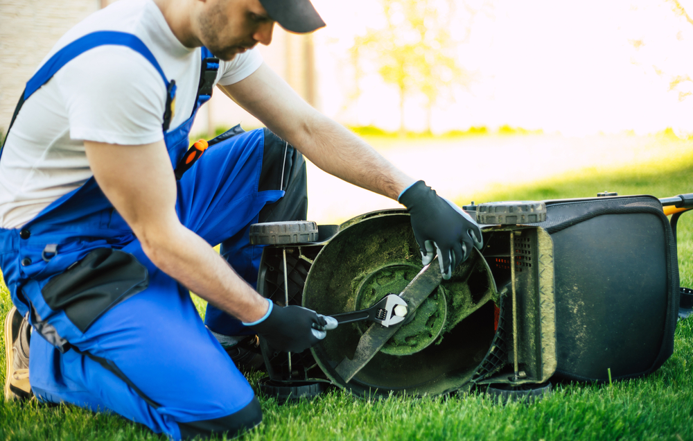 A man using a wrench to remove his lawn mower blade.