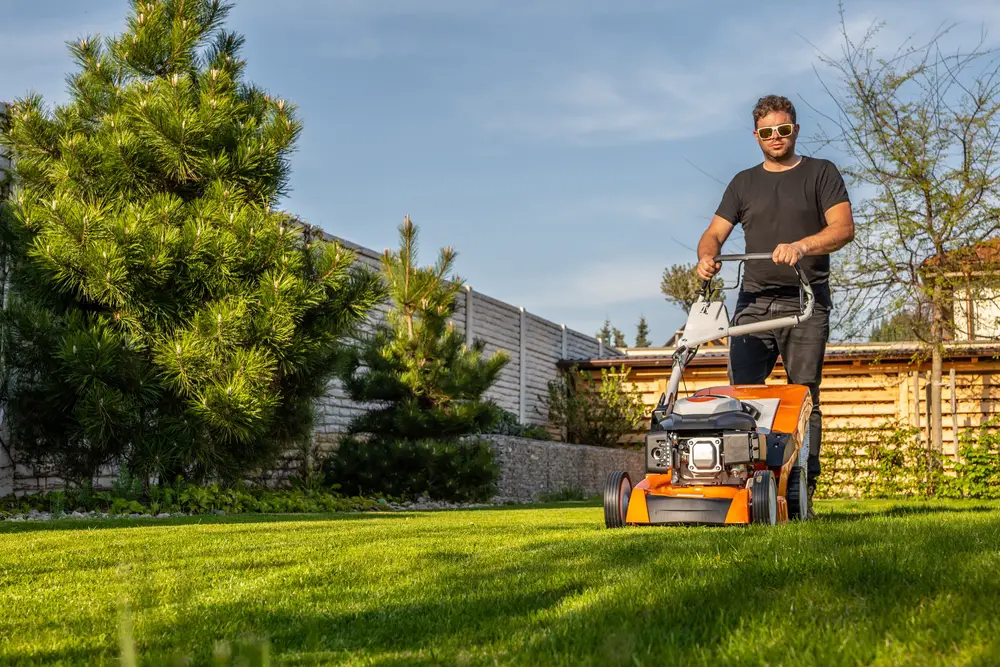 A man with sunglasses mowing his lawn.