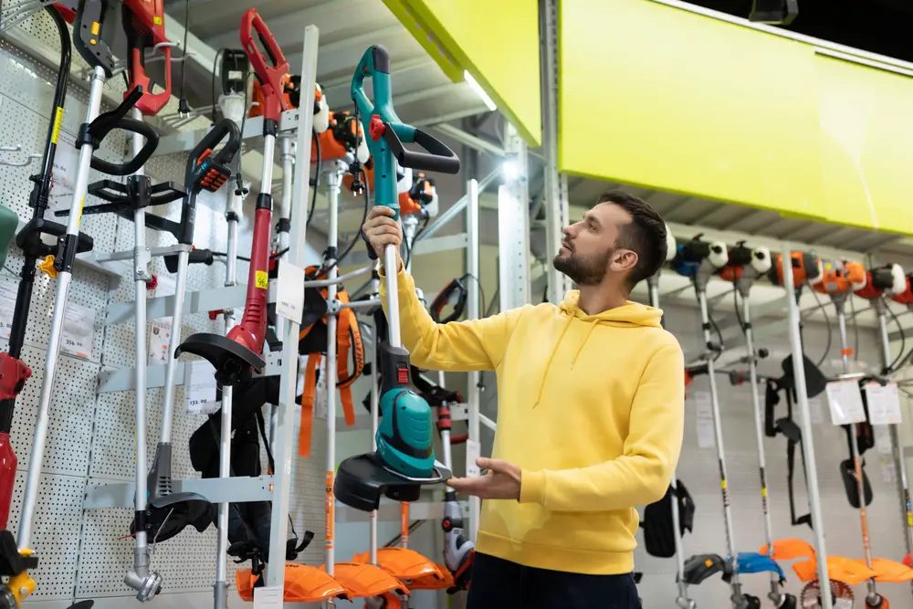 A man in a yellow hoodie examining a weed whacker.