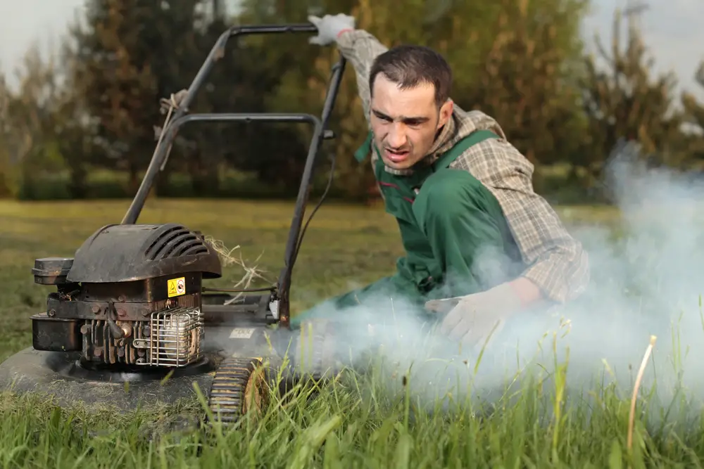 A man inspecting the smoking exhaust of his lawn mower.