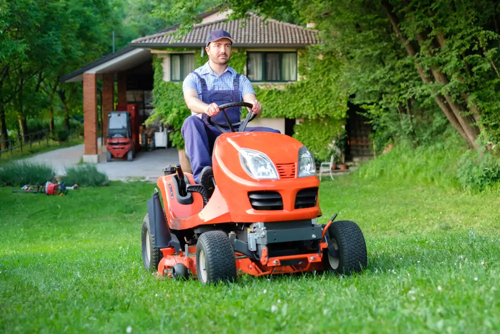 A man in overalls on an orange riding lawn mower cutting the grass.