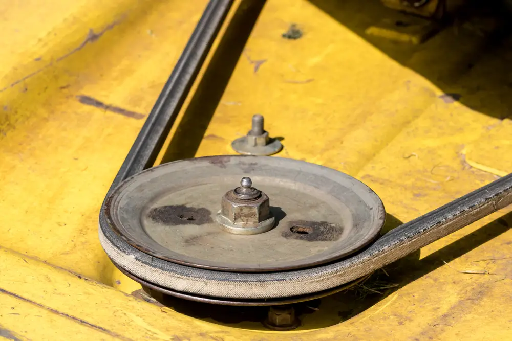 A closeup of a yellow lawn mower's pulley and belt.
