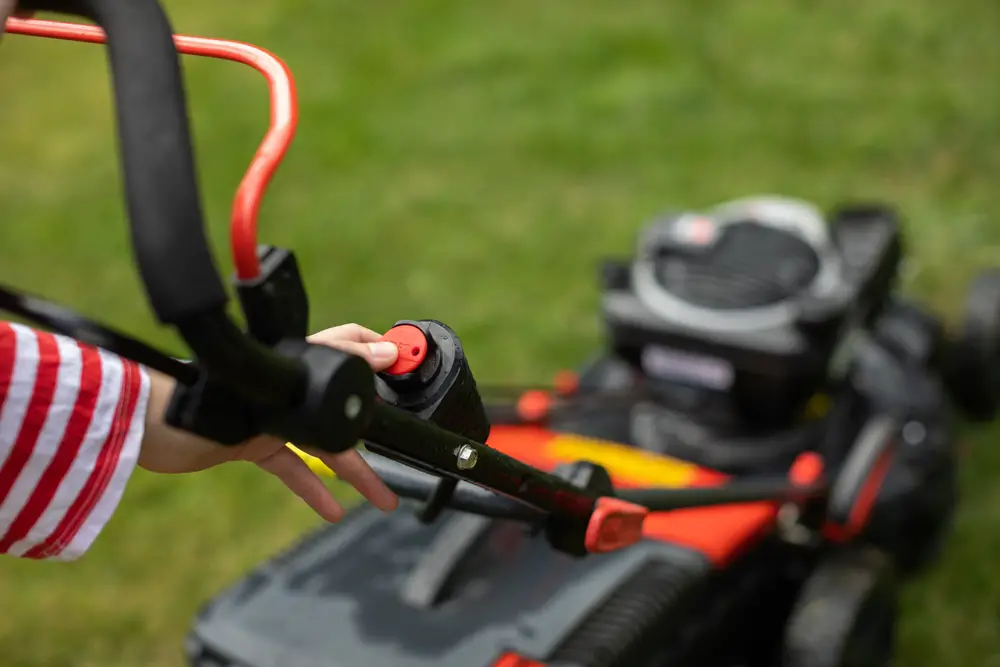 A closeup of a woman pushing a button on a lawn mower.