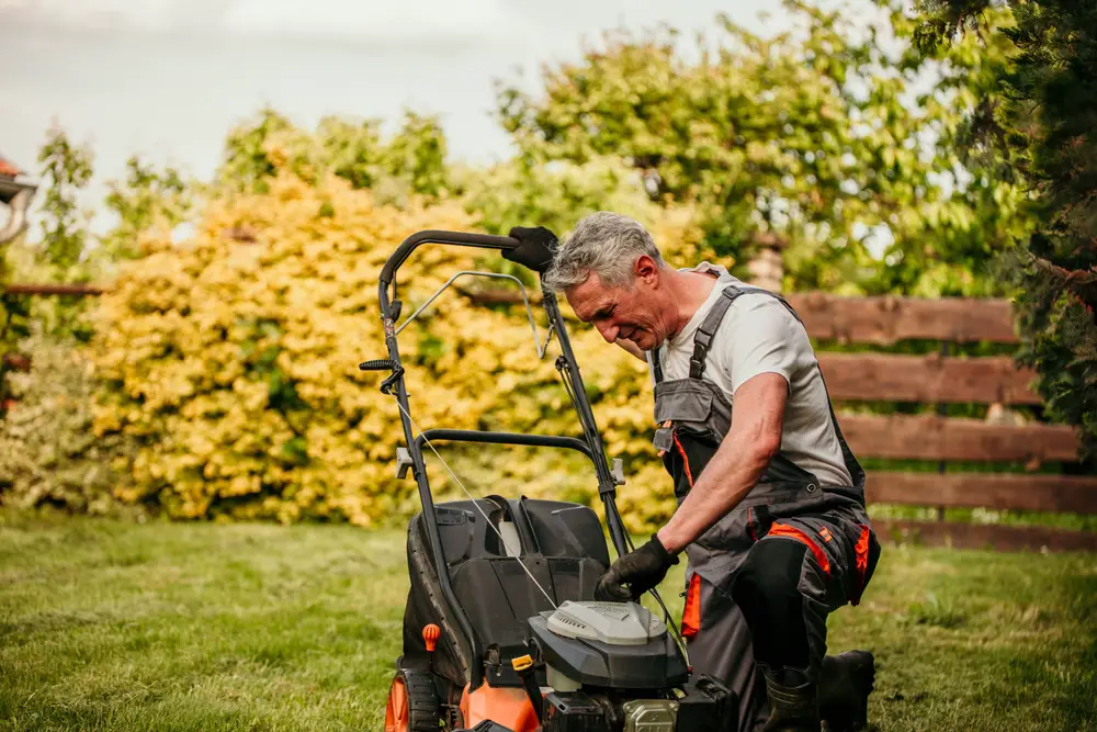 An older man checking his lawn mower, which is having an issue.
